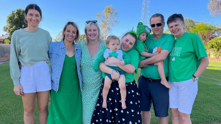 Six adults and a child dressed in green and smiling at the camera. 