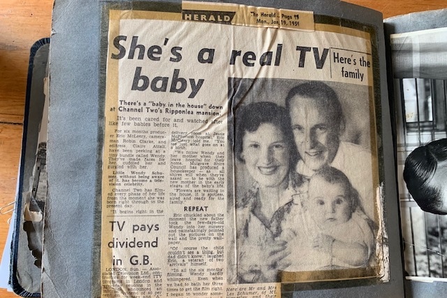 A photo shows a scrapbook open on a page with a newspaper clipping of a feature about the show Baby in the House
