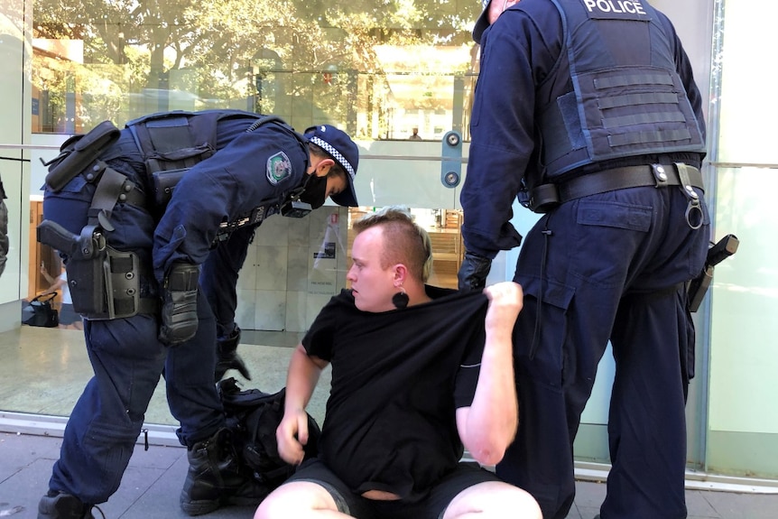 A man sits on the ground with a police officer on either side