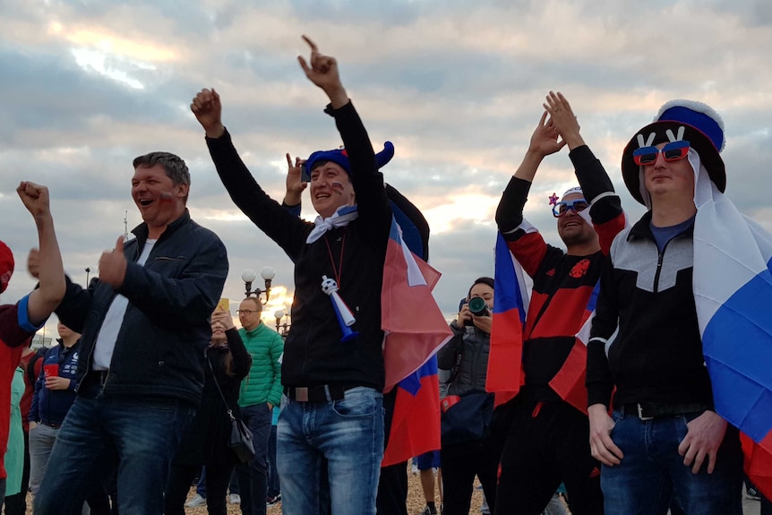 Fans dressed in blue white and red stand with hands raised, cheering