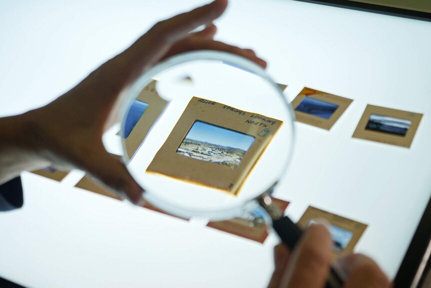 A photo of a magnifying glass held over a vintage slide showing Alice Springs.