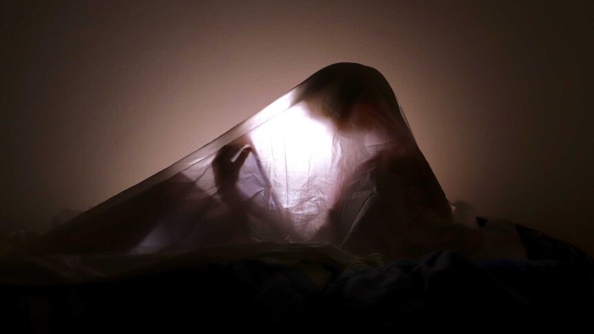 A child's shadow can be seen under a bed sheet, lit by a tablet's backlight.