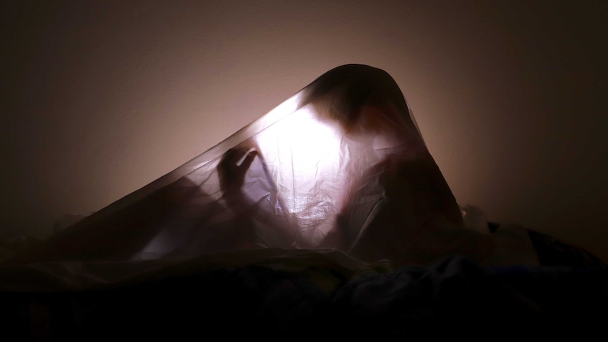 A child's shadow can be seen under a bed sheet, lit by a tablet's backlight.