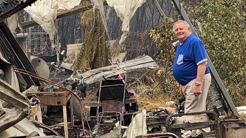 An older man in a blue shirt stands among the twisted ruins of his home after a fire in Victoria.