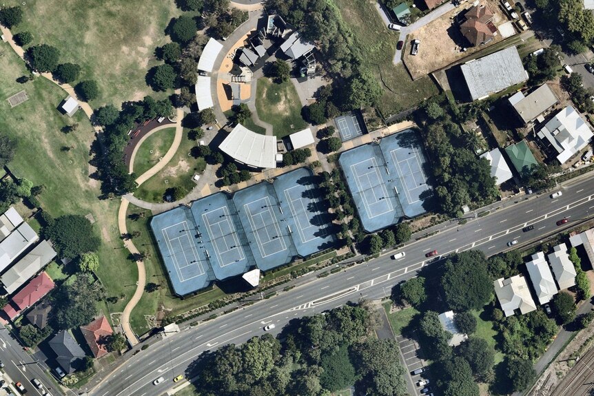A row of blue tennis courts and a large children's playground are seen from above.