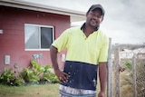 Aboriginal man leans on fence outside of family home.