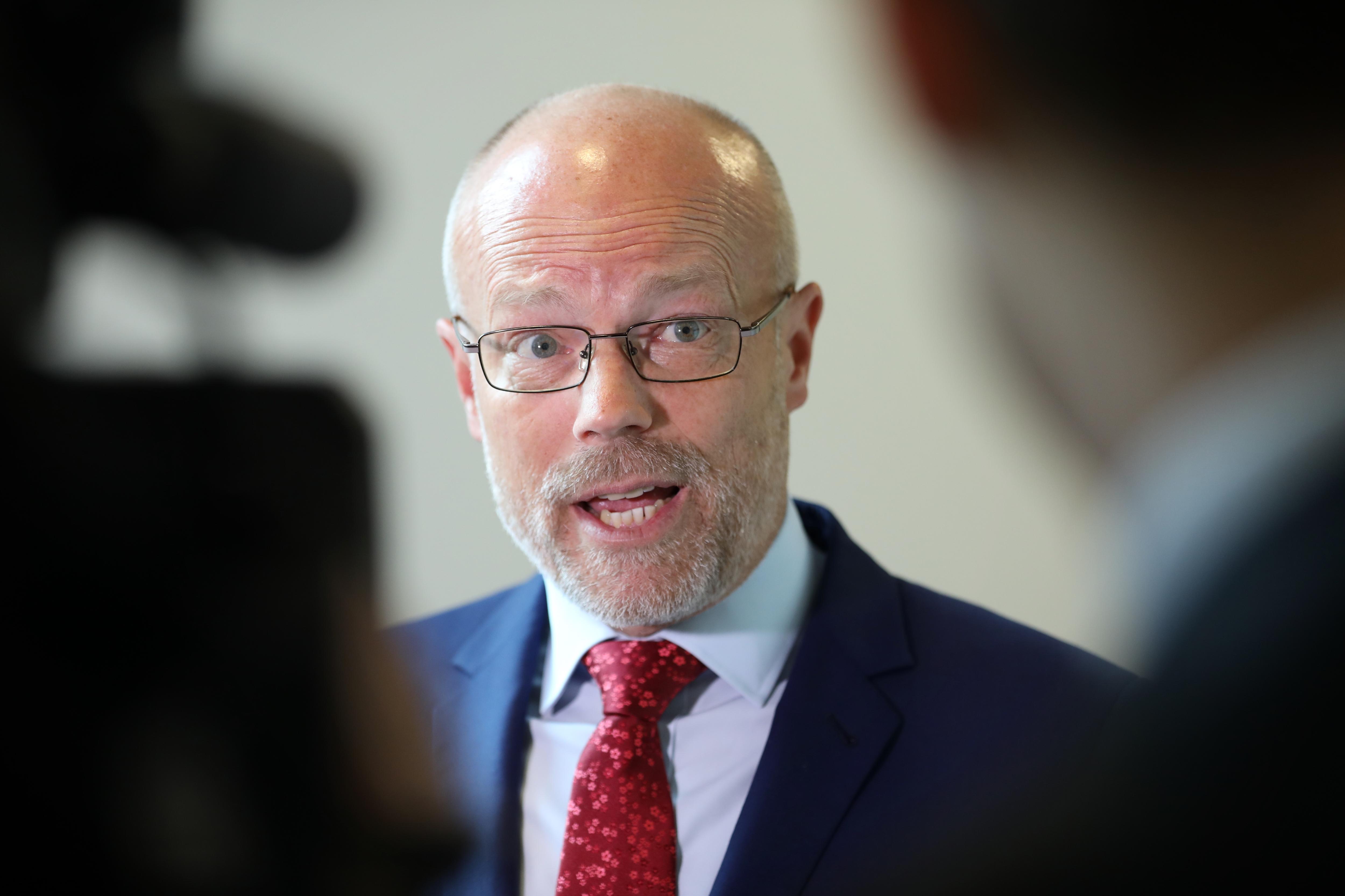 A bald man wearing glasses is speaking to silhouetted figures.