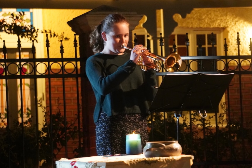 A girl playing trumpet at the front of a Perth house at dusk.