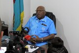 Fijian politician Sitiveni Rabuka sits at his desk surrounded by a media scrum