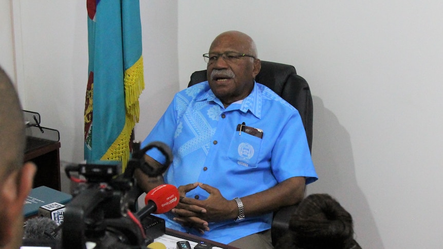 Fijian politician Sitiveni Rabuka sits at his desk surrounded by a media scrum