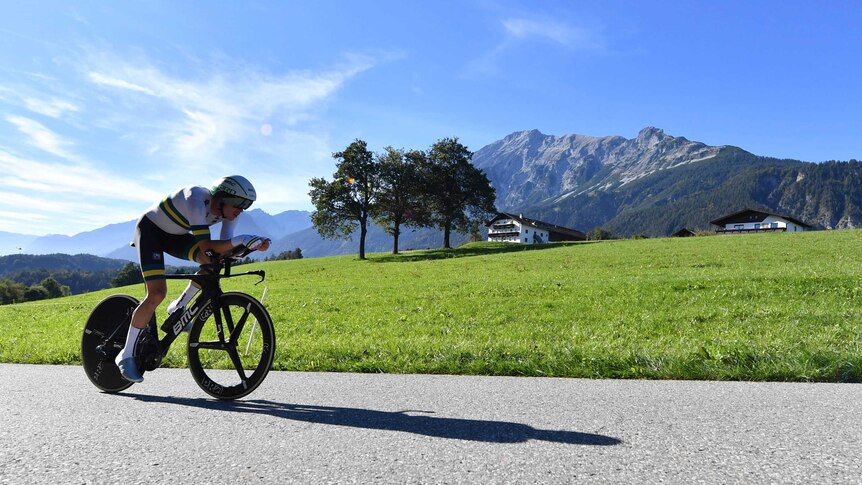 A cyclist rides a time trial bike along a road with a mountain in the background