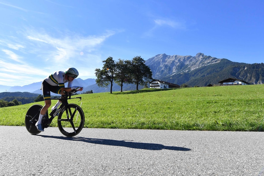 A cyclist rides a time trial bike along a road with a mountain in the background