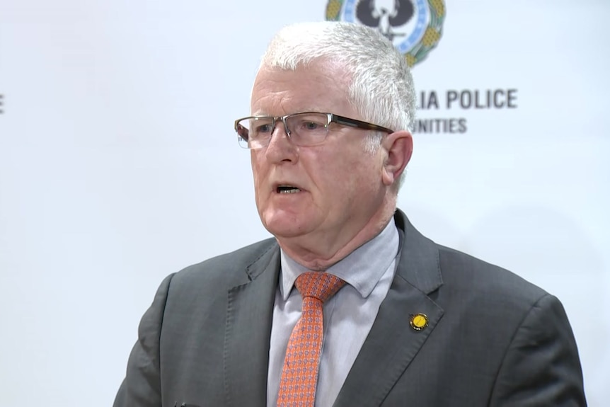 A man with glasses and in business suit speaking against police banner