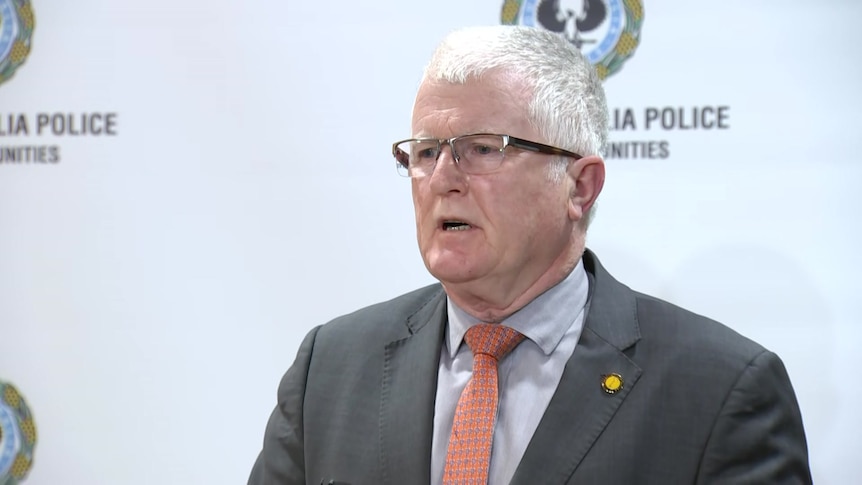 A man with glasses and in business suit speaking against police banner