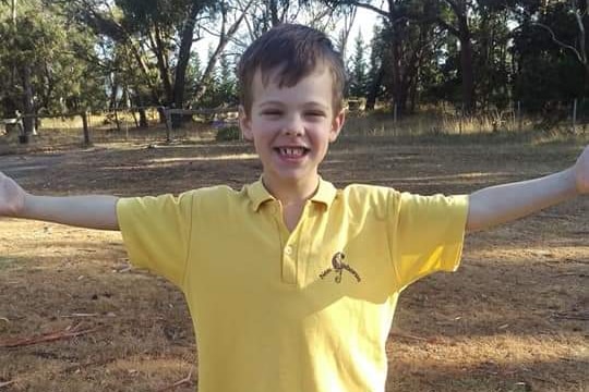 Young boy standing in a field, his arms outstretched. He is wearing a yellow polo shirt