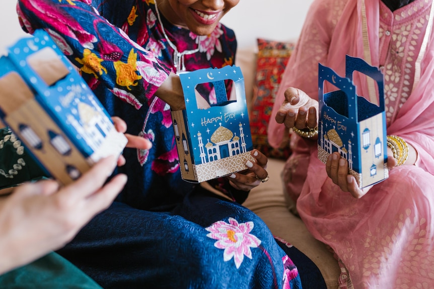 Three women each holding on to eid envelopes