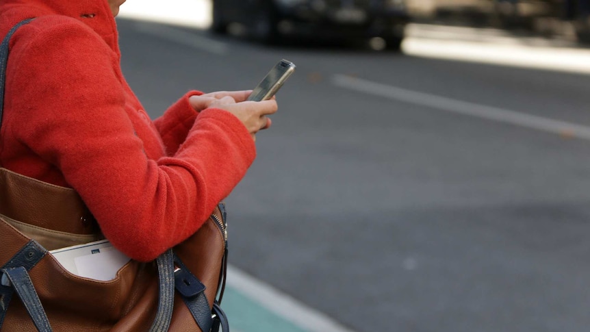 A woman holds a mobile phone while waiting to cross the road in Brisbane's CBD.