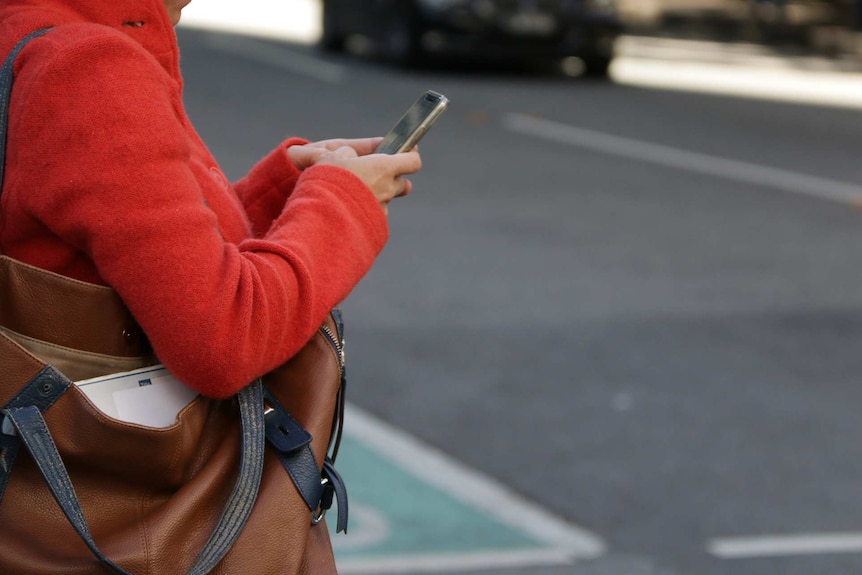 A woman holds a mobile phone while waiting to cross the road in Brisbane's CBD.
