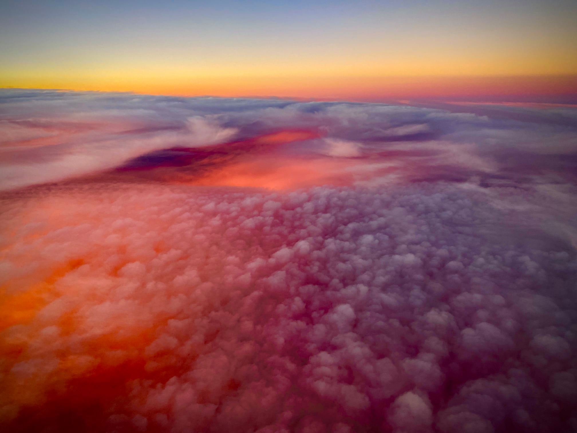 Photo of pink and orange clouds lit up from underneath, taken from a plane.