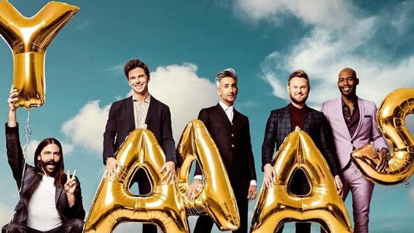 Five men pose with gold, balloon letters that spell YAAAS, standing against a cloudy sky