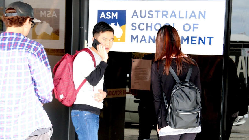 Students stand outside the Perth campus of Careers Australia, reading a notice in the window.