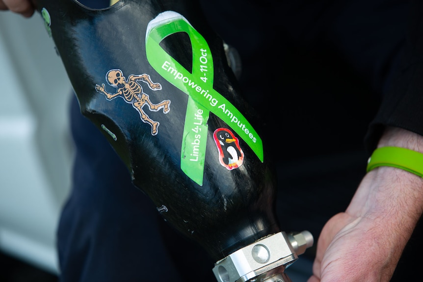 A black prosthetic leg with stickers on it  -  a skeleton, a penguin and the message 'empowering amputees'