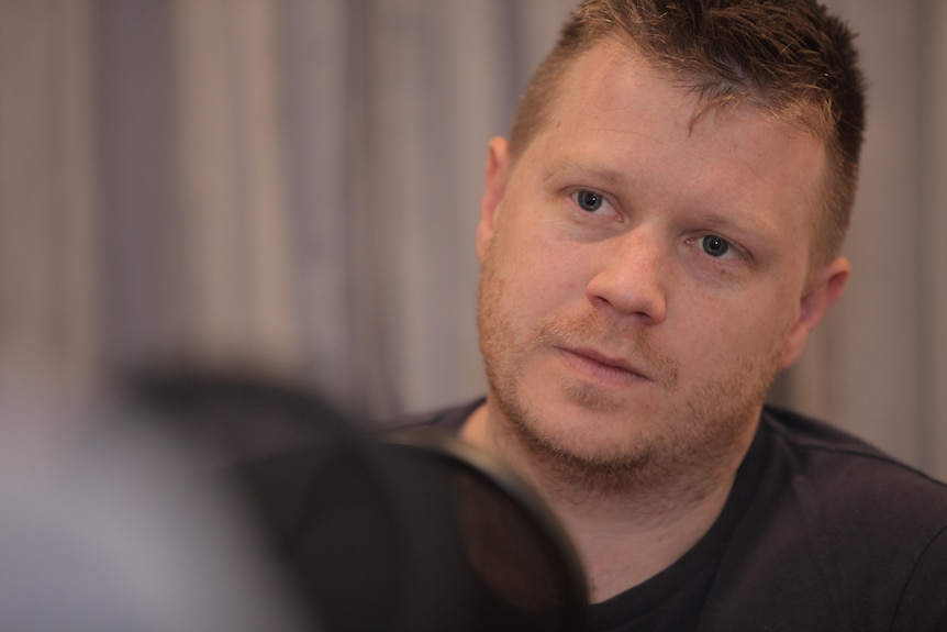 A close up of a man sitting in front of microphone