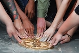 A bronze plaque being touched by the hands of several people.