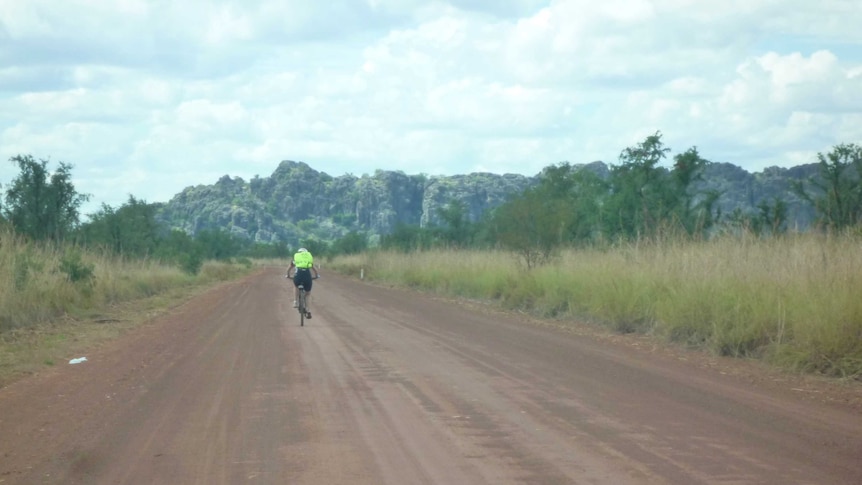 A cyclist in fluro yellow on a dirt road with distant grey mountains