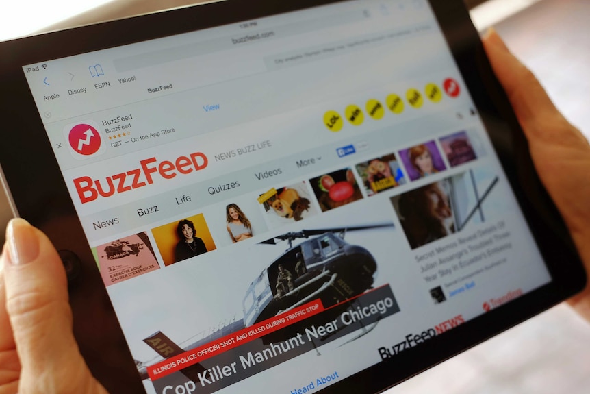 A person holding an iPad with the Buzzfeed website displayed.