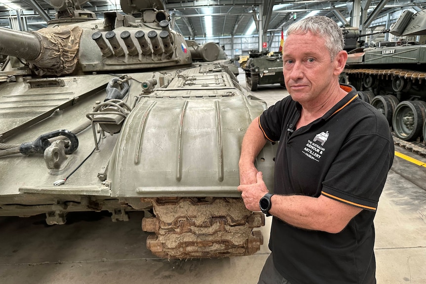 A man leans against a tank in a museum. 