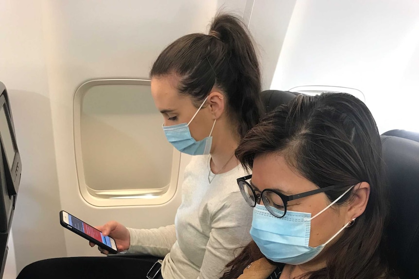Two female passengers sitting next to each other on a Qantas flight, wearing masks.