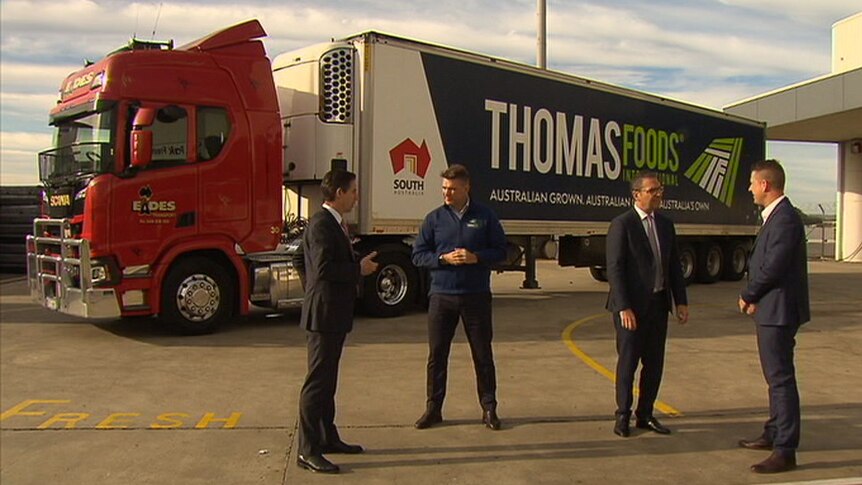 Four men standing far apart talking in front of a truck with the words Thomas Foods on it