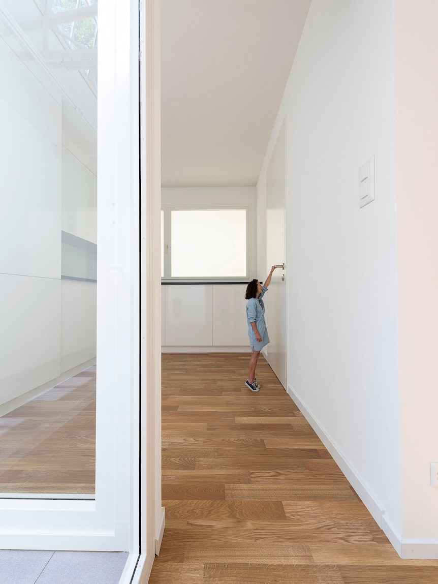 A white apartment with a woman reaching up to a far too large door