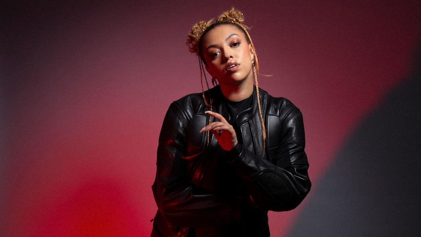 Mahalia is in a black leather coat and her hair back with a red gradient background