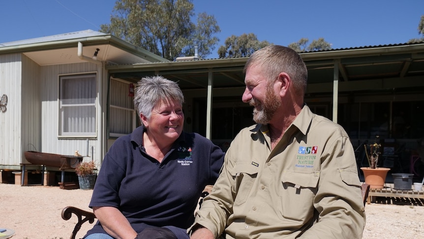 Colleen and Peter Barnes smiling at each other while sitting on a bench in front of their home at Neds Corner