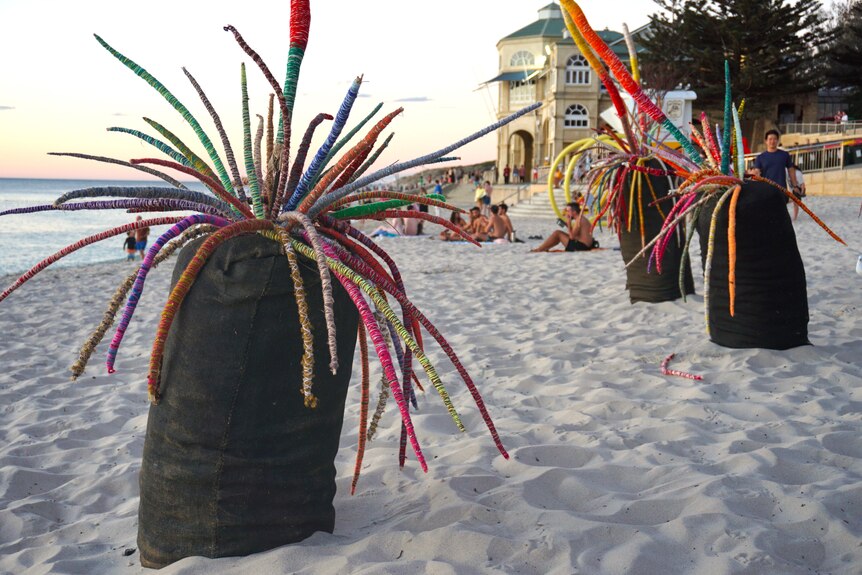 Several grass tree sculptures made from yarn are pictured on the sand at Cottesloe beach. 