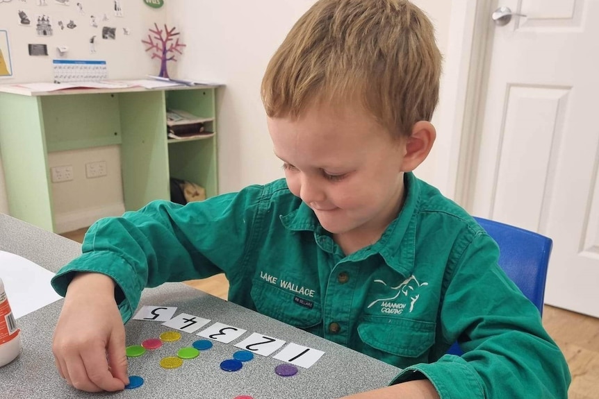 A young boy wearing a green shirt sitting at a table working with numbers and tokens