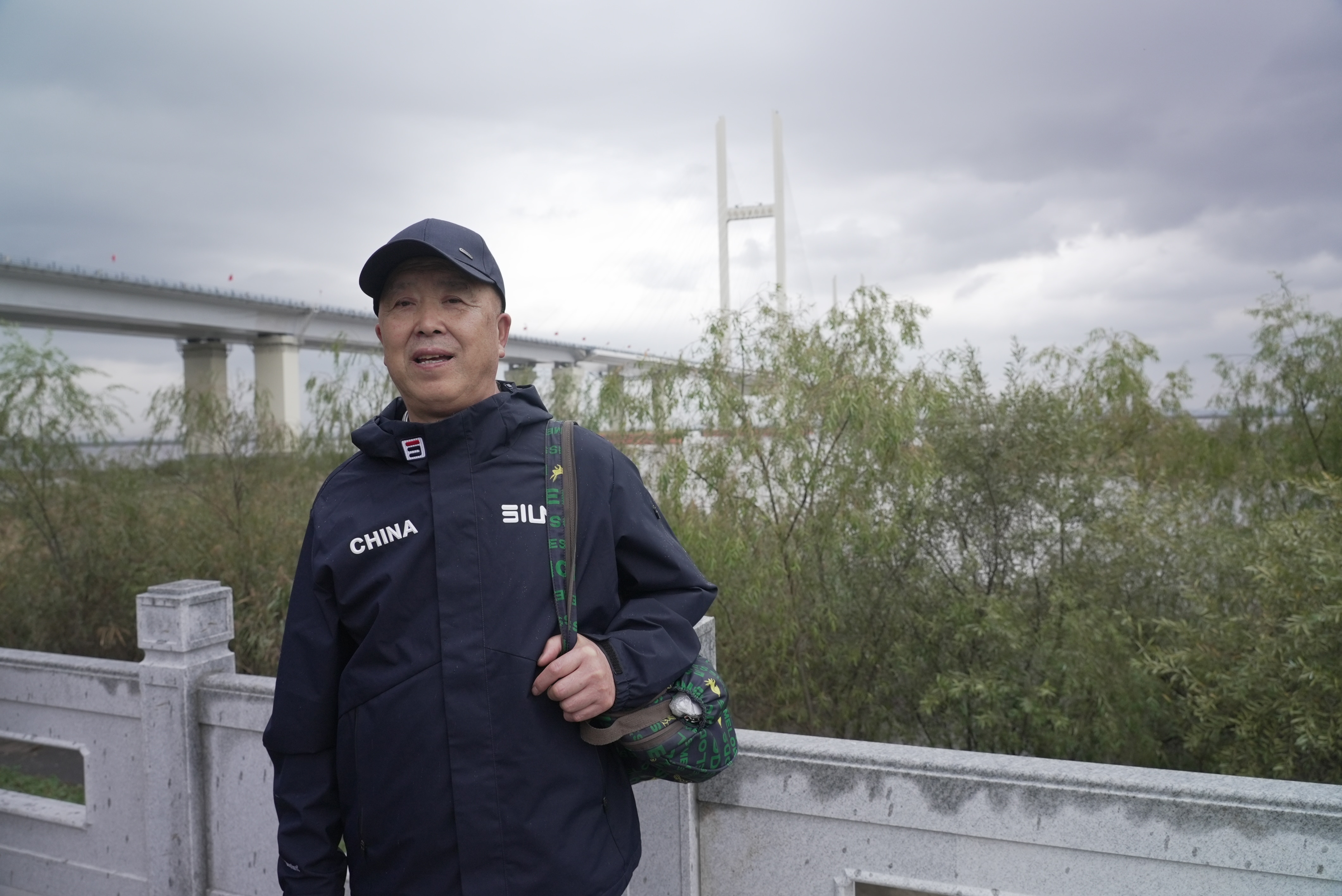 Mr Yang stands beside a guardrail on a riverbank.