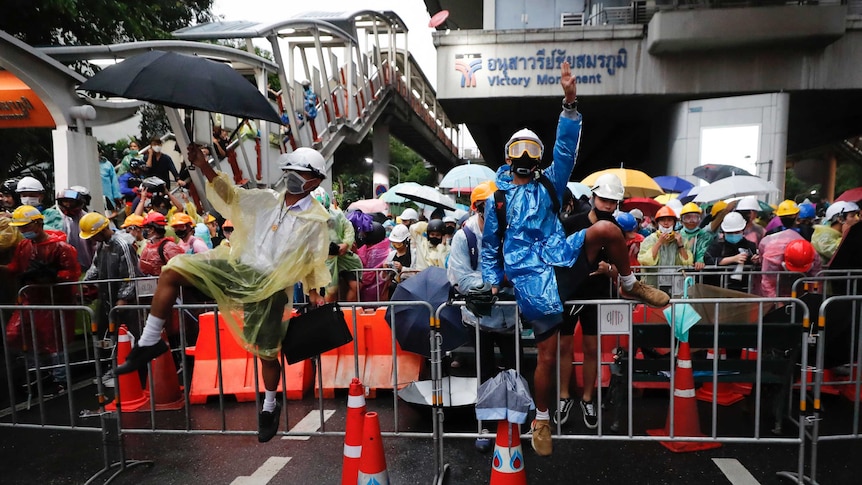 Pro-democracy protesters, dressed in colourful raincoats and with umbrellas, try and cross a barrier in Bangkok.