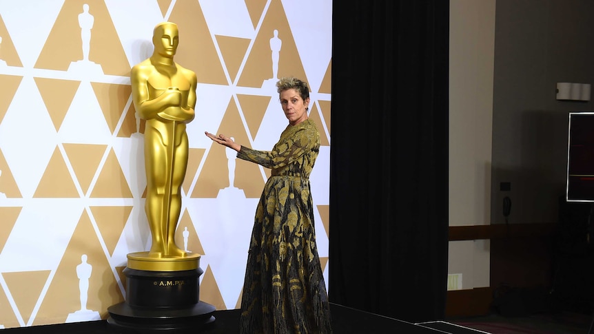 Frances McDormand poses next to an Oscar statue.
