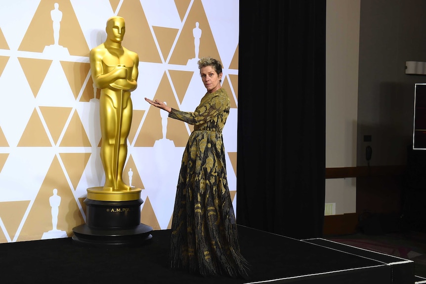 Frances McDormand poses next to an Oscar statue.