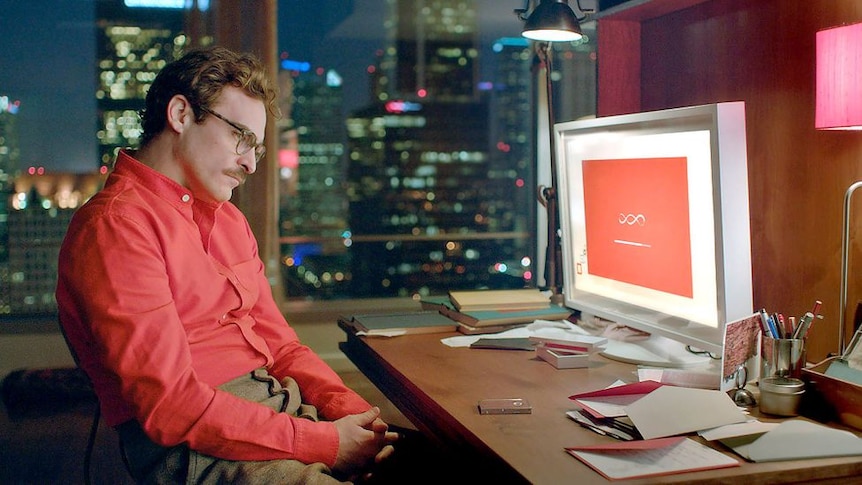 Actor Joaquin Phoenix is sitting down starring at a computer, which is his artificial intelligent girlfriend, from the movie Her
