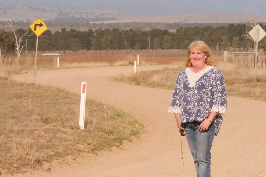 A woman stands on a gravel road looking towards the camera.