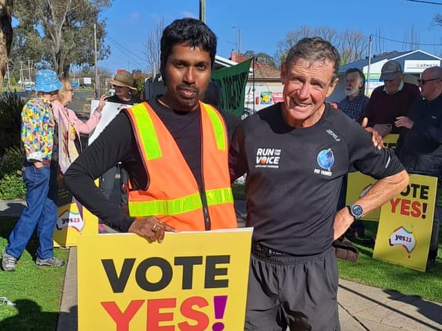 Two men stand in front of a crowd holding a sign that reads vote yes