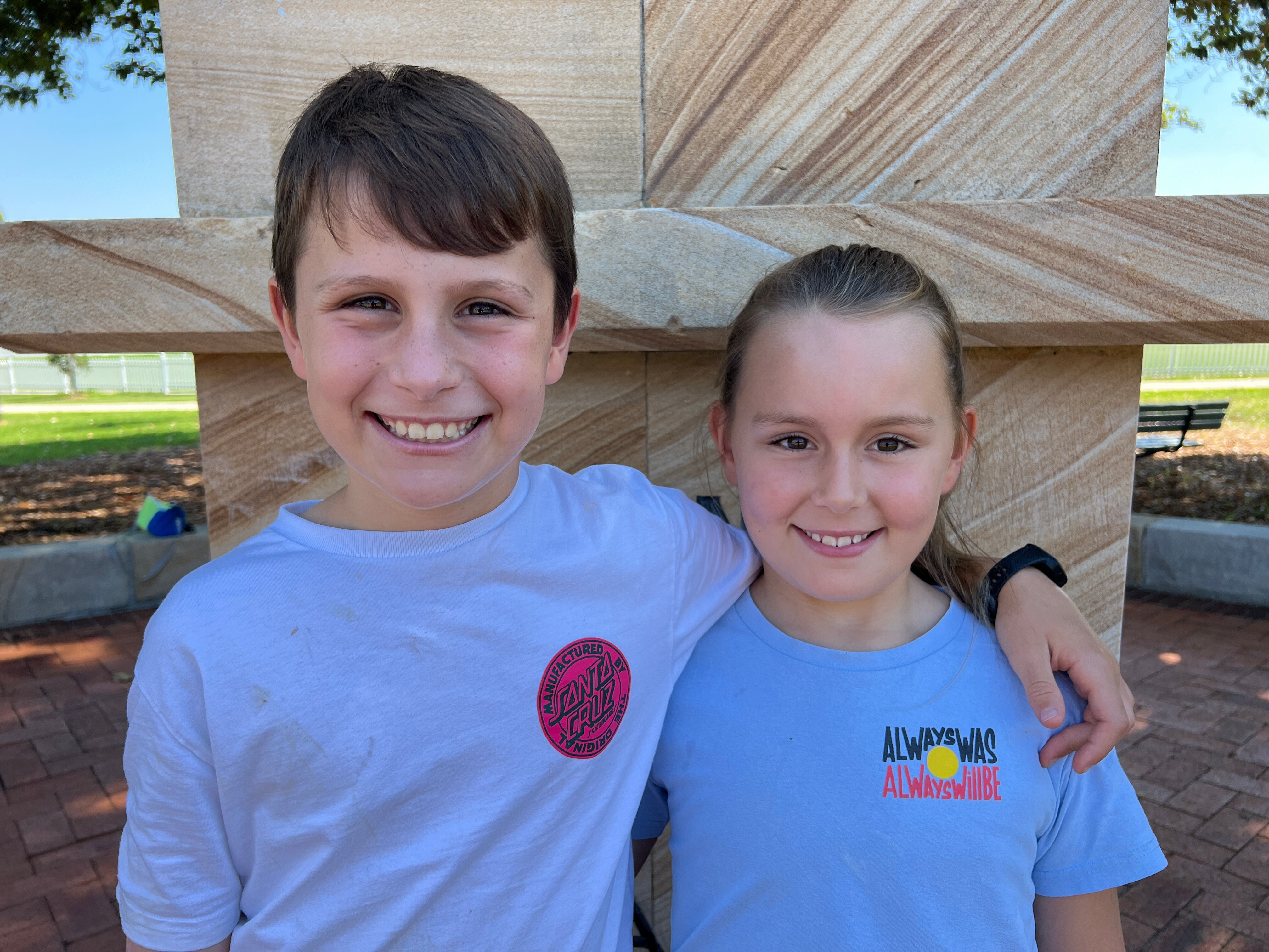 A photo of a young boy with his arm around his younger sister. They both have brown hair and brown eyes.