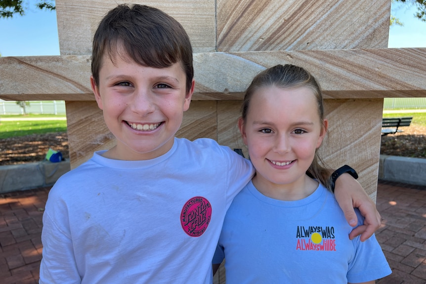 A photo of a young boy with his arm around his younger sister. They both have brown hair and brown eyes.