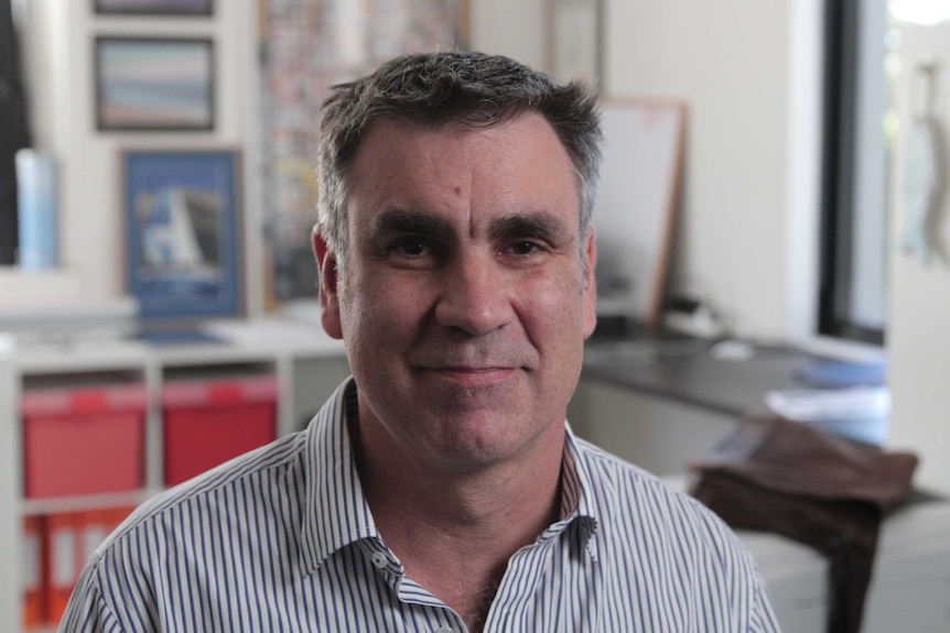 A man sitting in his office with desk and storage in the background.