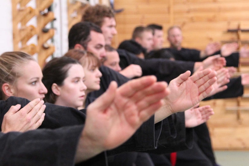 Adults stand in a line with their hands up at the ready during a ninja training class at Bujinkan Tasmania Budo Dojo in Hobart.