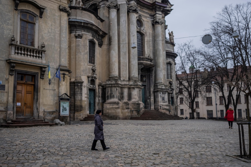 A woman walks on cobblestones past an old museum.